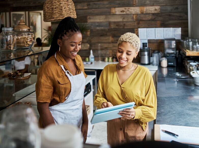 two women in a bakery smiling, one of them holding a tablet in her hands