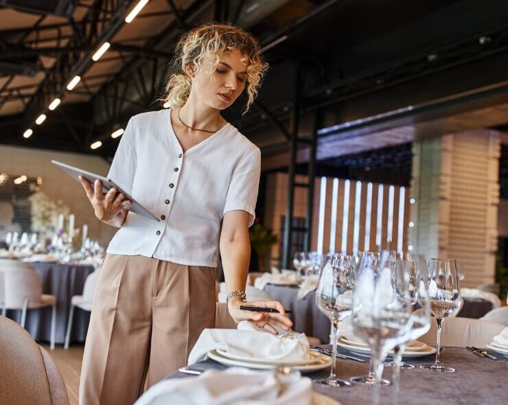blonde woman, supervising the tables at an event, she is holding a tablet in her hands.