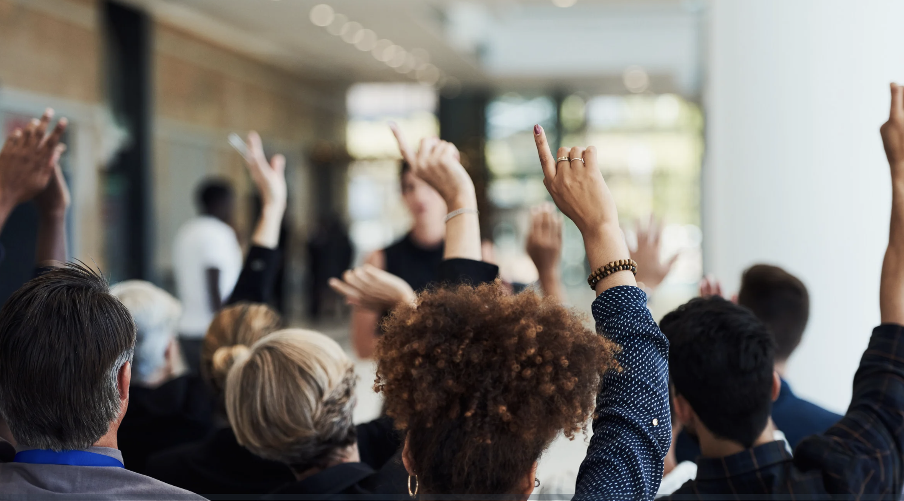 Group of people sit in a room for a ticketed event, raising their hands.